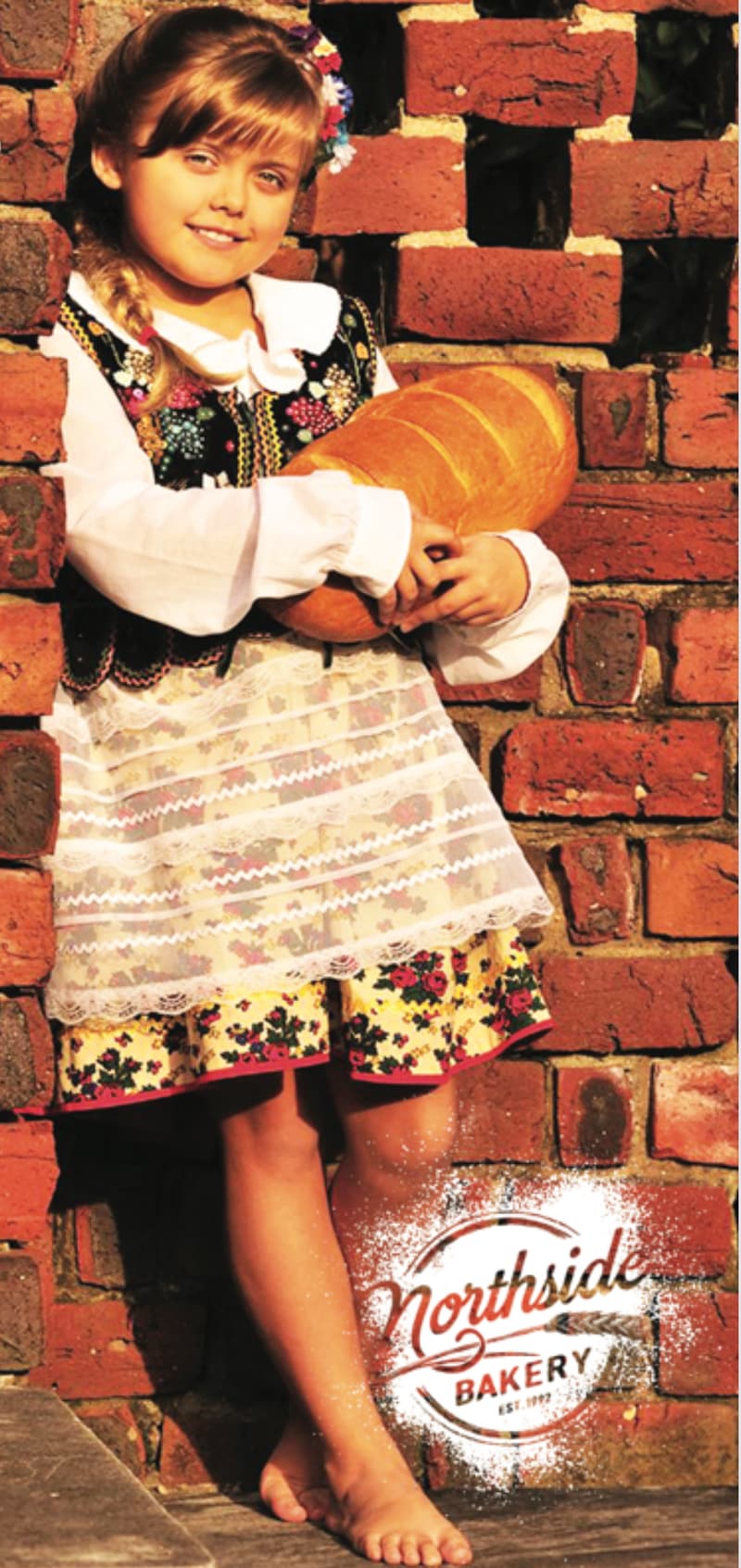 Old Northside Bakery poster: a girl in Polish folk dress holding a big loaf of bread against a brick wall