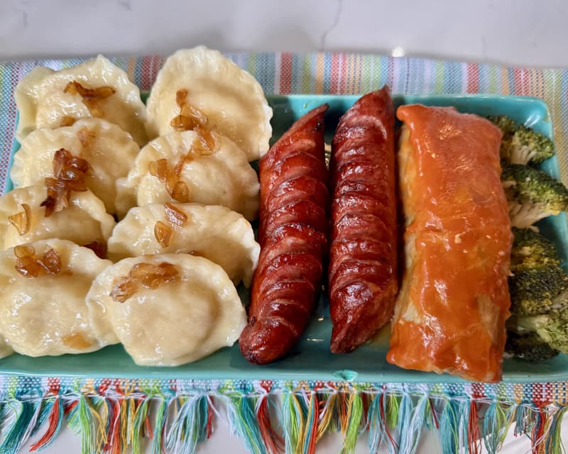 A platter of pierogi with fried onions and grilled kielbasa