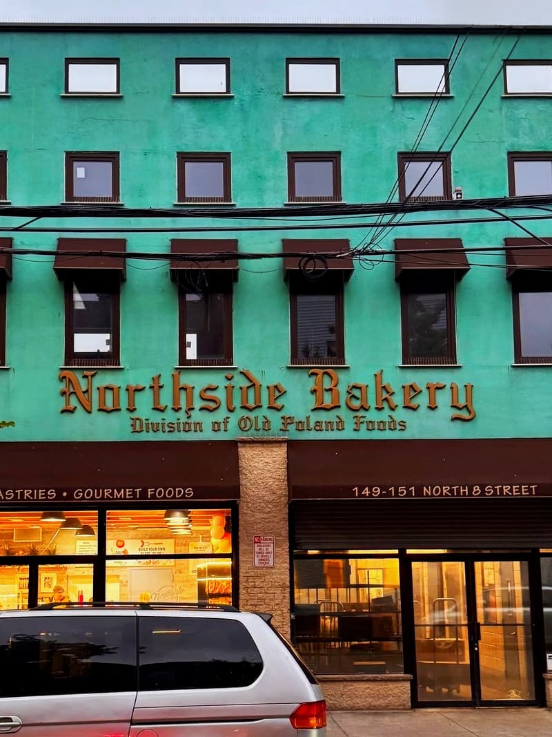 The teal Northside Bakery building on North 8th Street, windows lit at dusk
